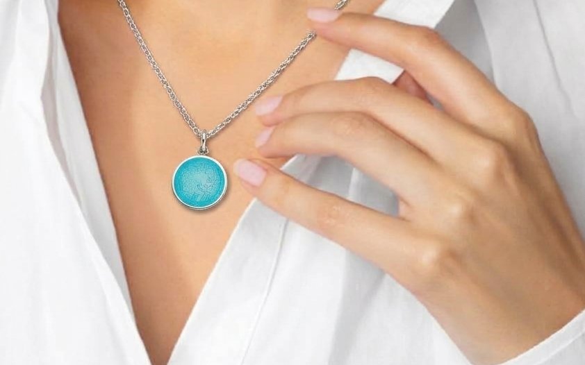 Woman in a white shirt wearing a light blue enamel St. Christopher medal on a silver chain