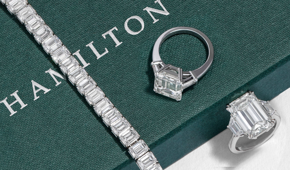 Diamond tennis bracelet and emerald-cut diamond rings on a green Hamilton box