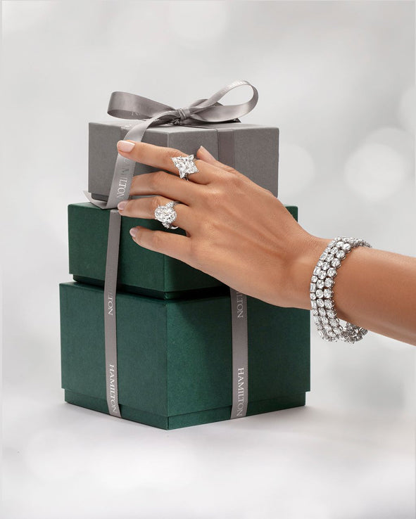 Hamilton gift boxes tied with silver ribbon, held by a hand wearing a diamond bracelet