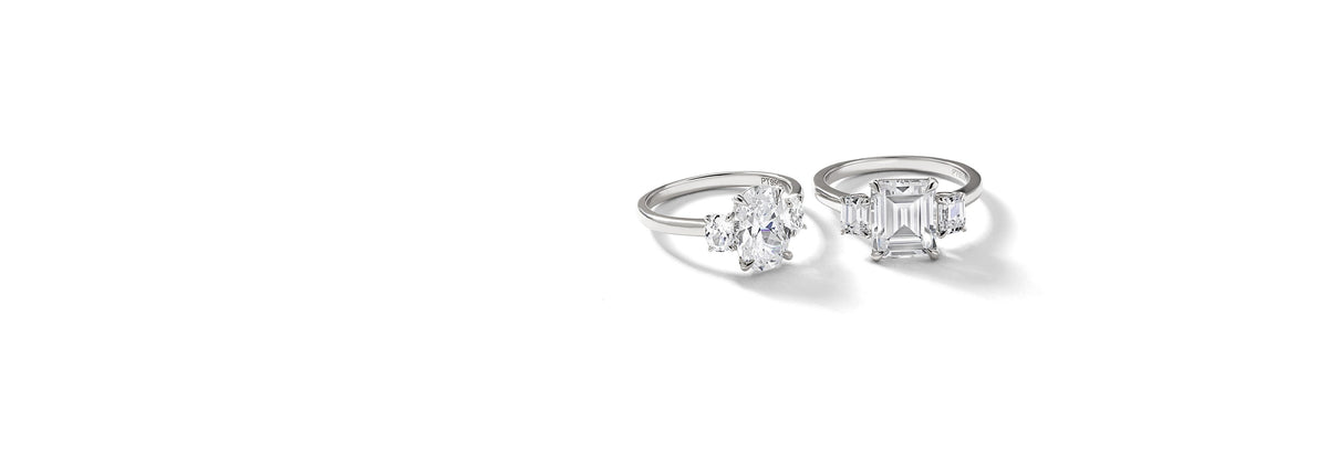 Two platinum diamond engagement rings — an oval three-stone and an emerald-cut three-stone