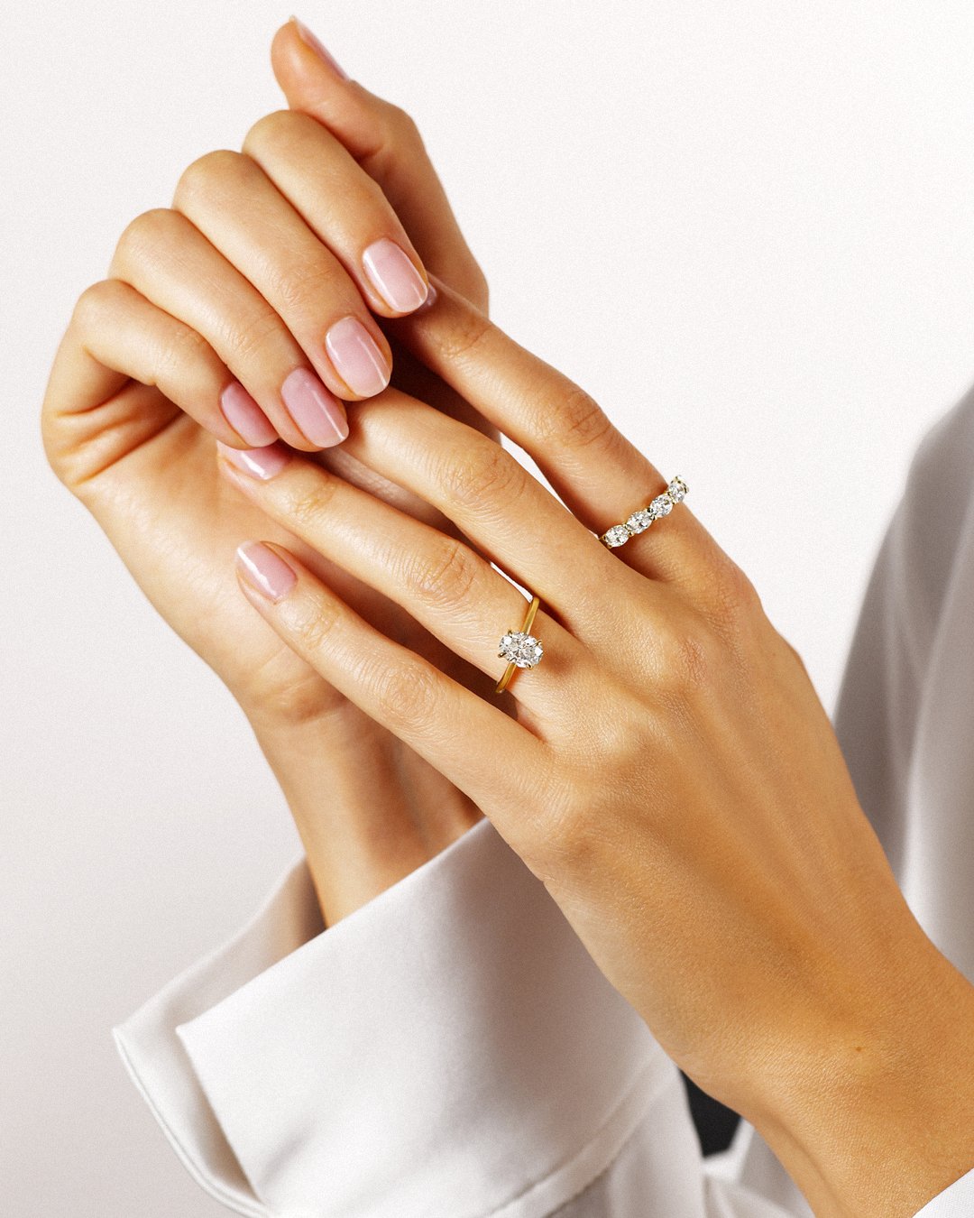 Hands wearing a round diamond solitaire engagement ring stacked with a diamond eternity band