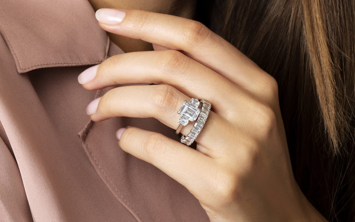 Close-up of a hand wearing an emerald-cut diamond engagement ring stacked with a diamond eternity band