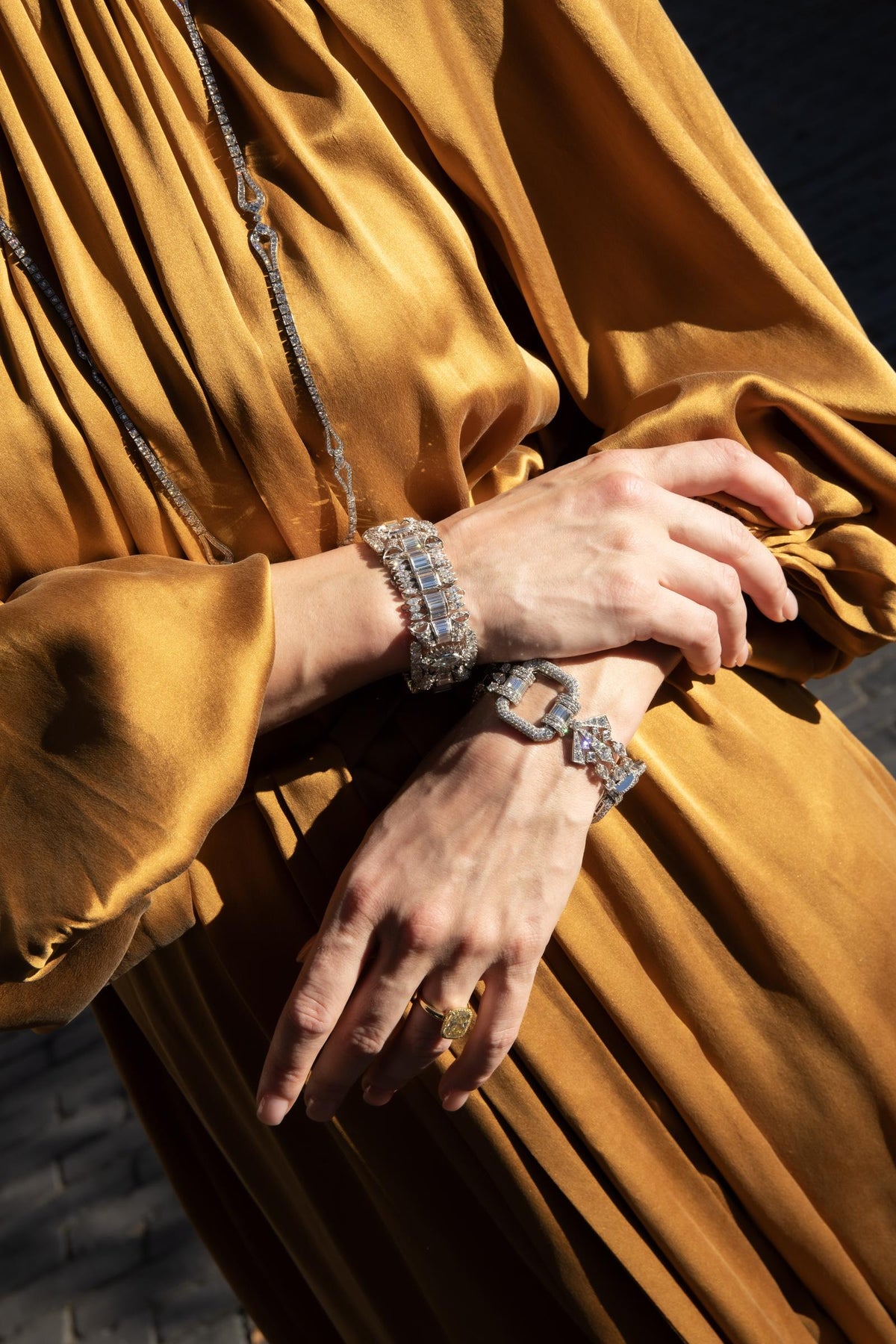 Woman in a gold satin dress wearing a wide diamond bracelet, a diamond link bracelet and a long diamond chain necklace