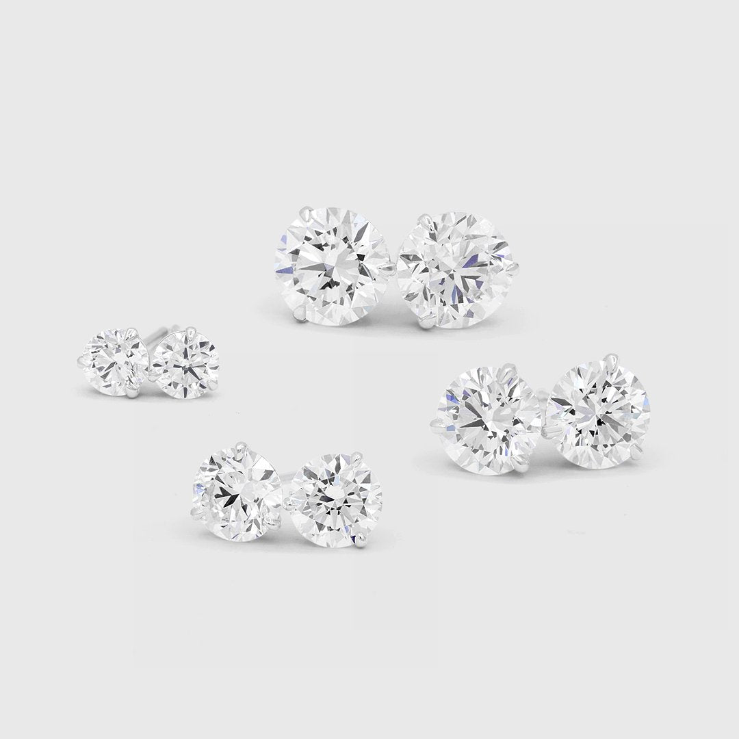 Four pairs of round diamond stud earrings in graduated carat weights on a light gray background