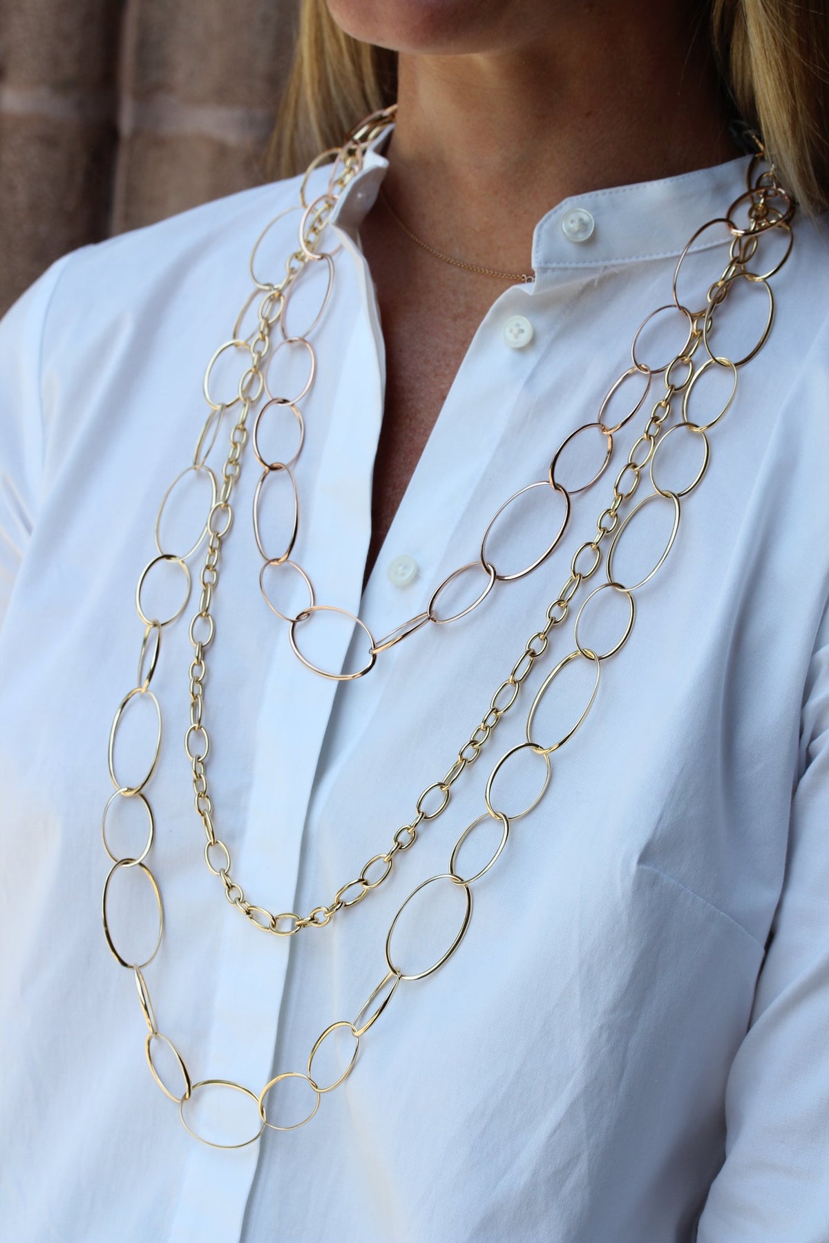 Woman in a white shirt wearing three layered yellow gold oval link chain necklaces