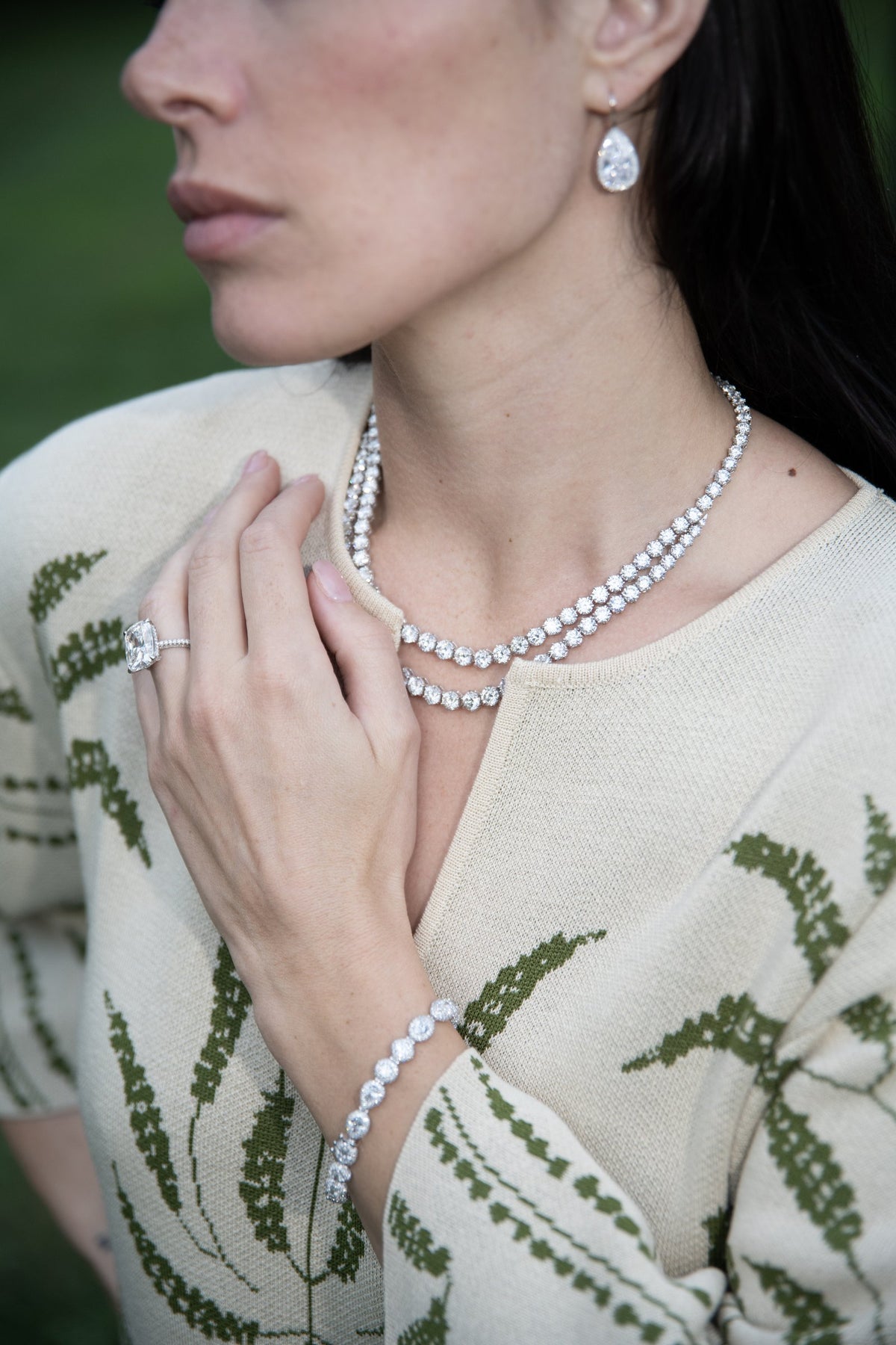 Woman in a cream patterned jacket wearing a two-row diamond riviera necklace, pear-shaped diamond drop earrings and a tennis bracelet