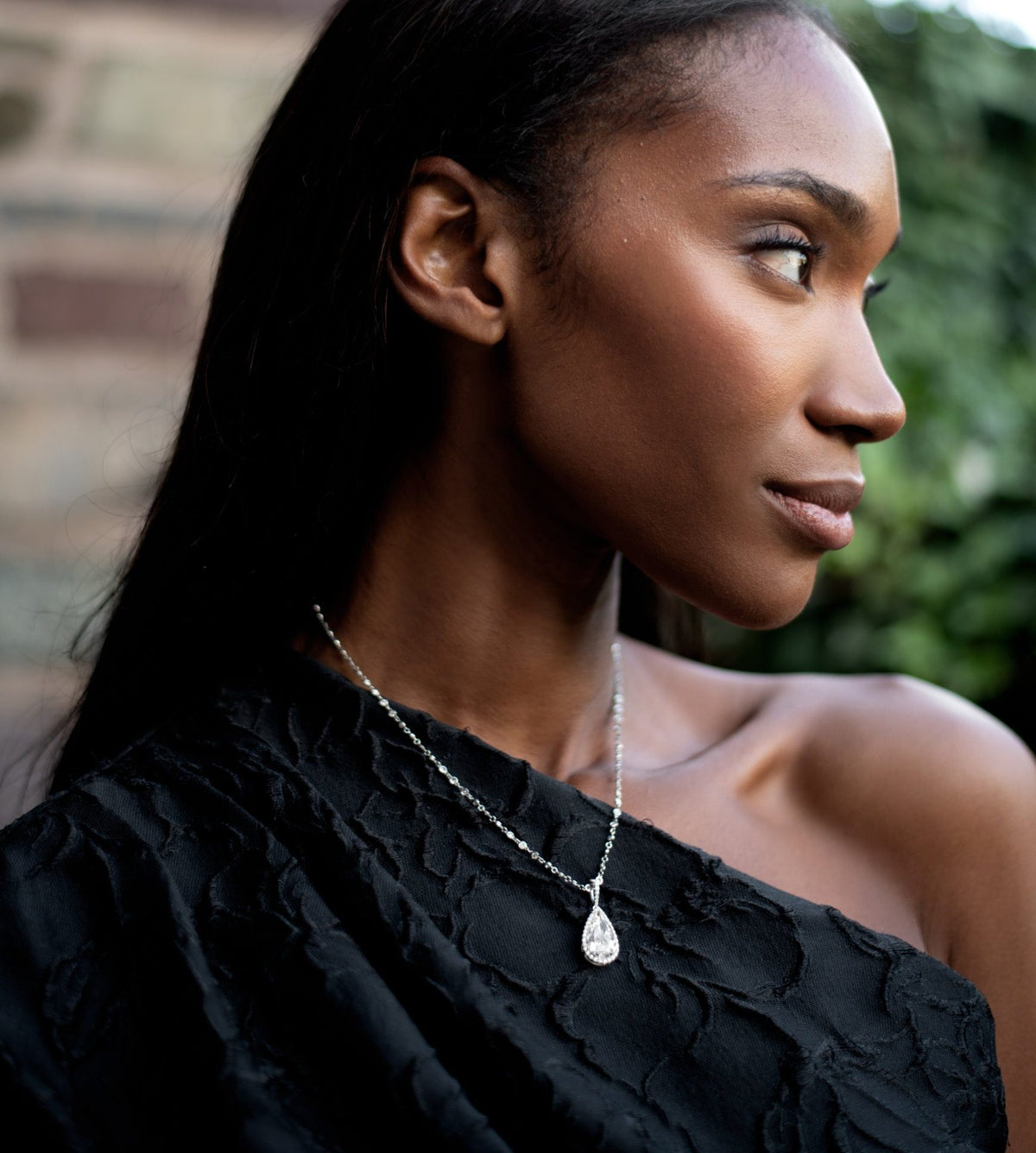 Woman in a black one-shoulder top wearing a white gold pear-shaped diamond pendant on a diamond station chain