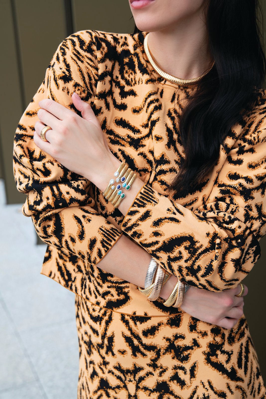 Woman in a leopard-print top wearing stacked gold cuffs and bangles and a gold collar necklace
