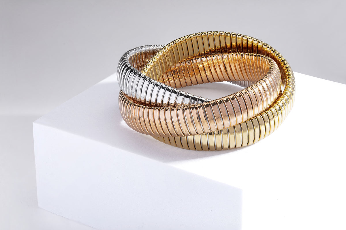 Three interlocking tubogas bangles in yellow, rose and white gold on a white block