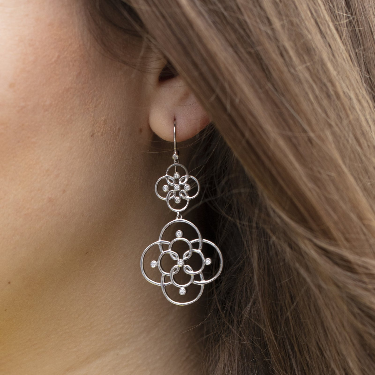White gold Arabesque openwork drop earring with diamonds worn by a woman with long brown hair
