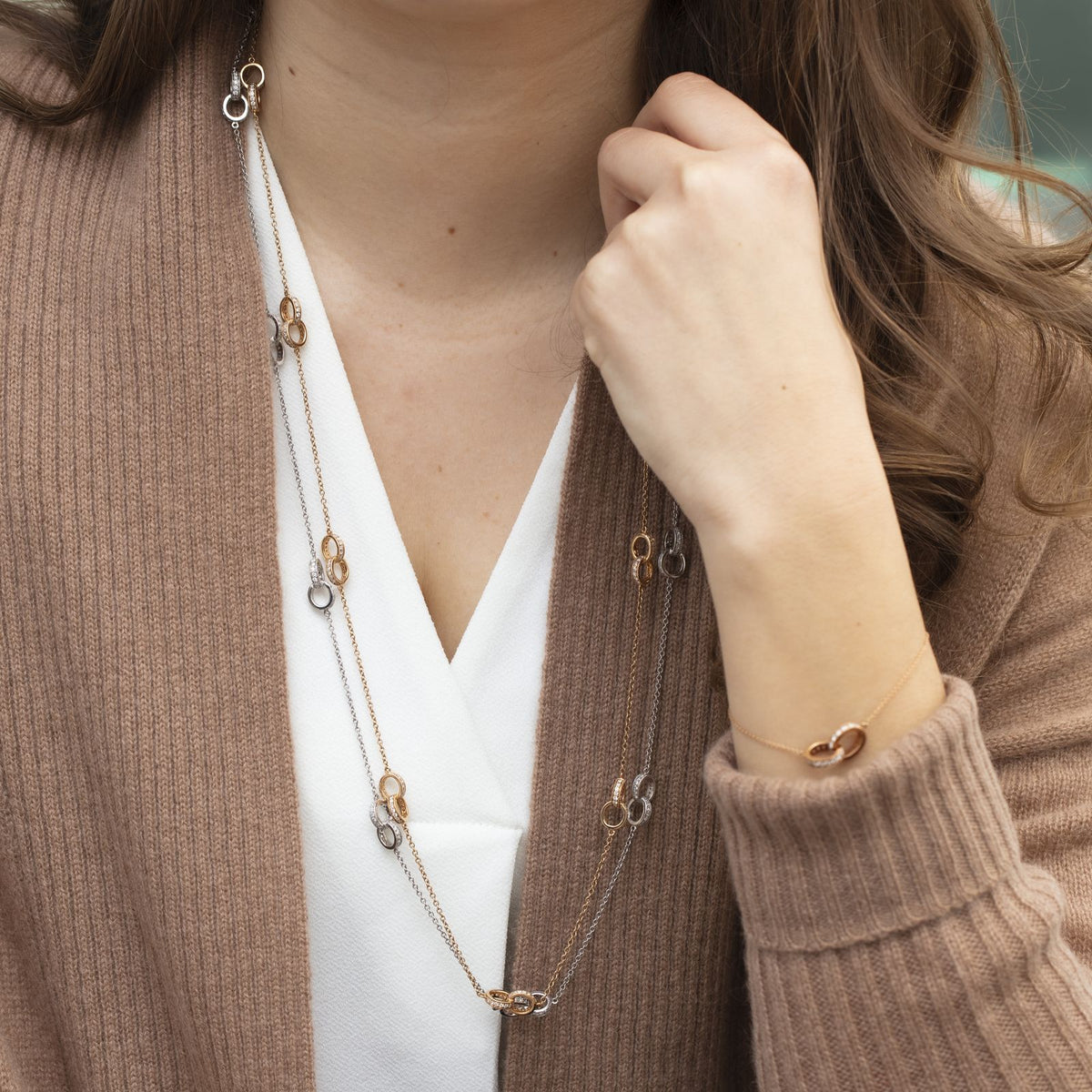 Woman in a camel cardigan wearing a long two-tone gold Eternity station necklace and matching bracelet