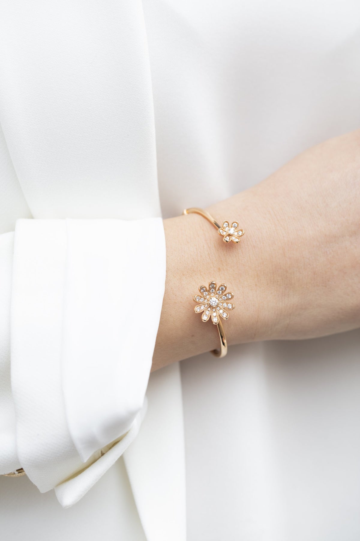 Rose gold Fleur flower cuff bracelet with diamond petals on a wrist, against a white blouse