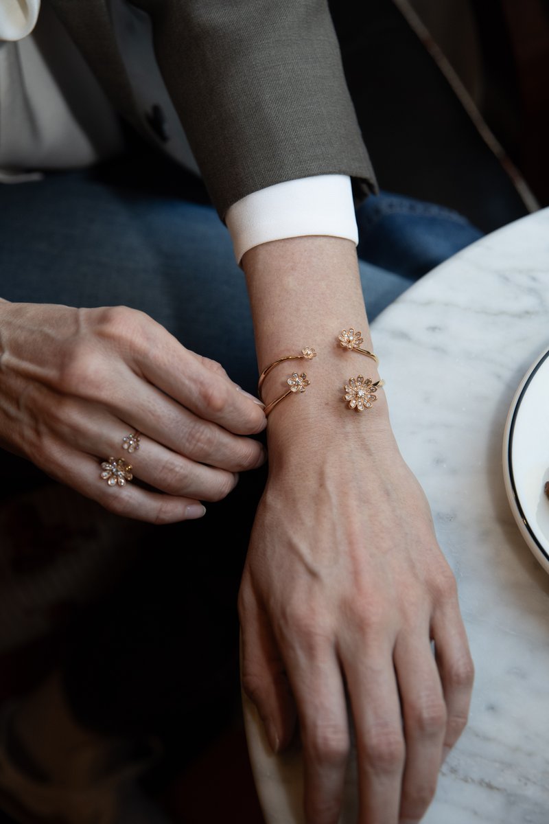 Woman in a navy blazer wearing a gold Fleur flower cuff and ring, hands resting on a marble table