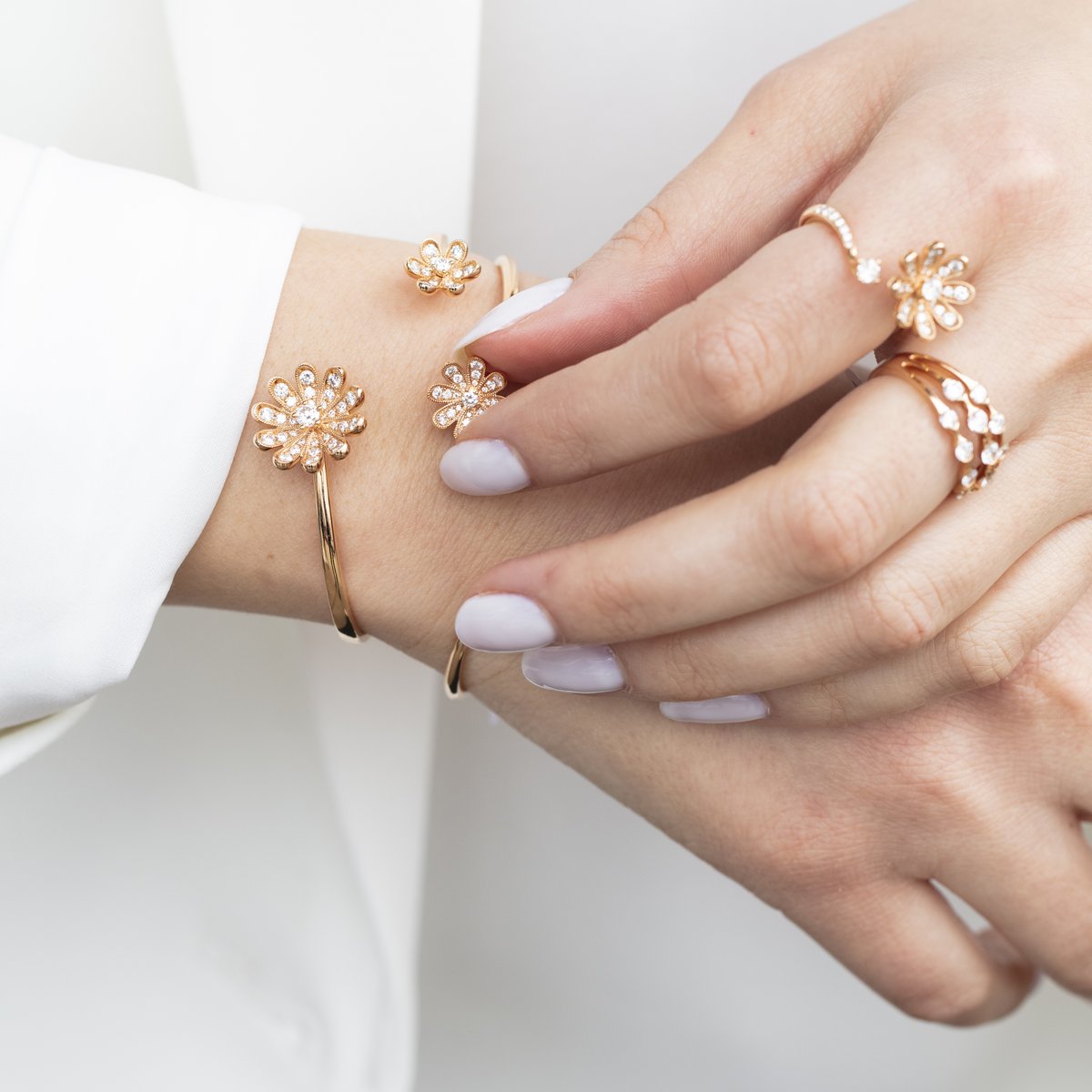 Hands wearing rose gold Fleur diamond flower rings and an open flower cuff