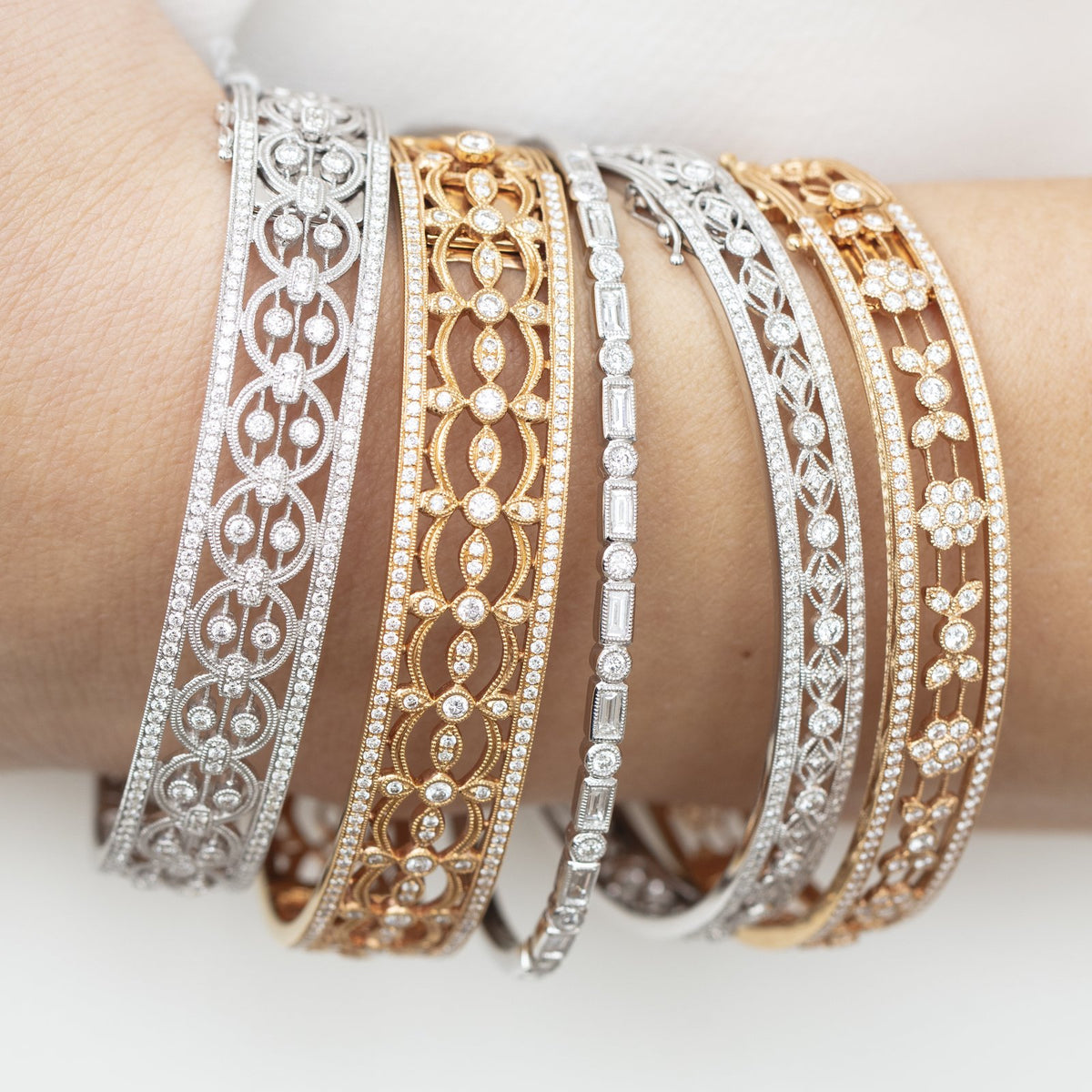 Five Heritage bangles in white, yellow and rose gold with diamond openwork patterns stacked on a wrist