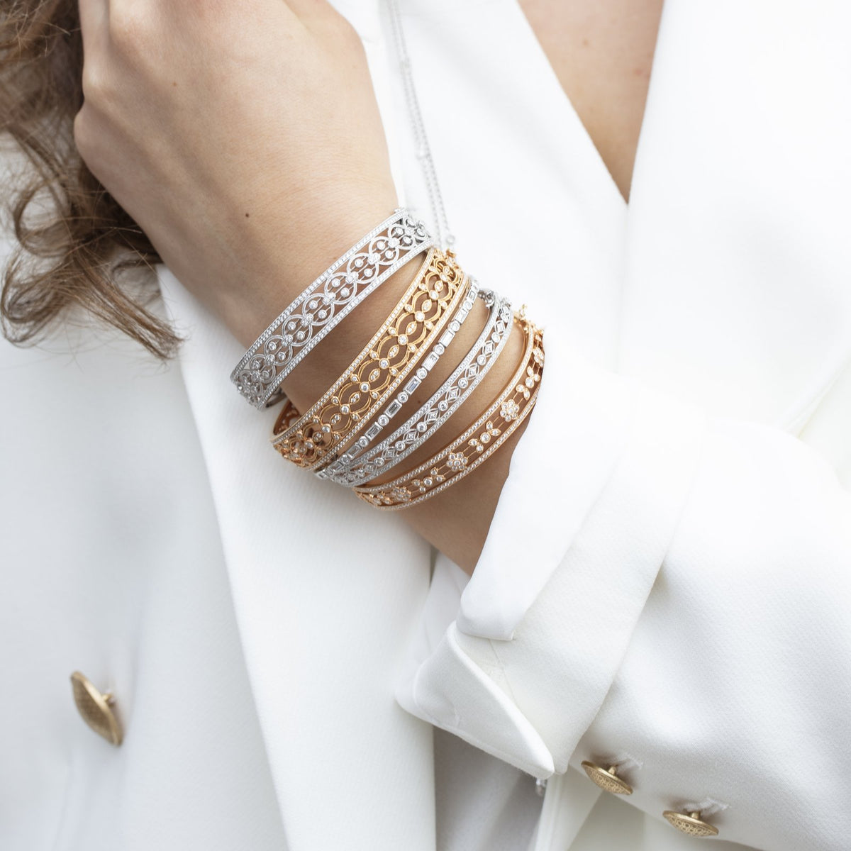 Woman in a white suit with a stack of mixed-gold Heritage diamond bangles on her wrist