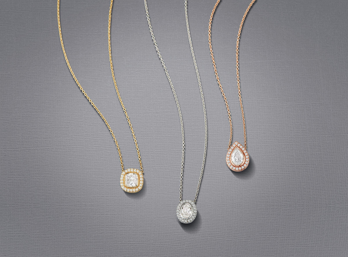 Three Lisette diamond halo pendants — cushion in yellow gold, oval in white gold and pear in rose gold — on chains against a gray background