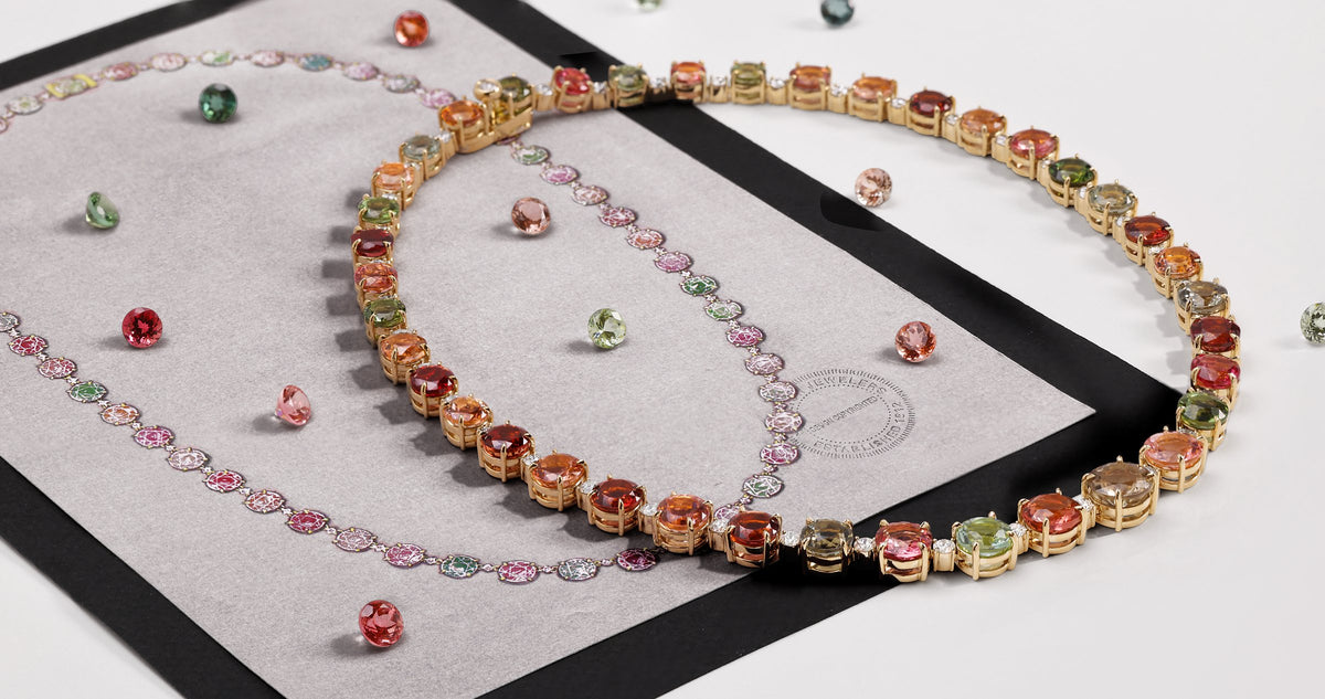 Multicolor sapphire and gemstone riviera necklace in yellow gold laid on a sketch with loose colored stones