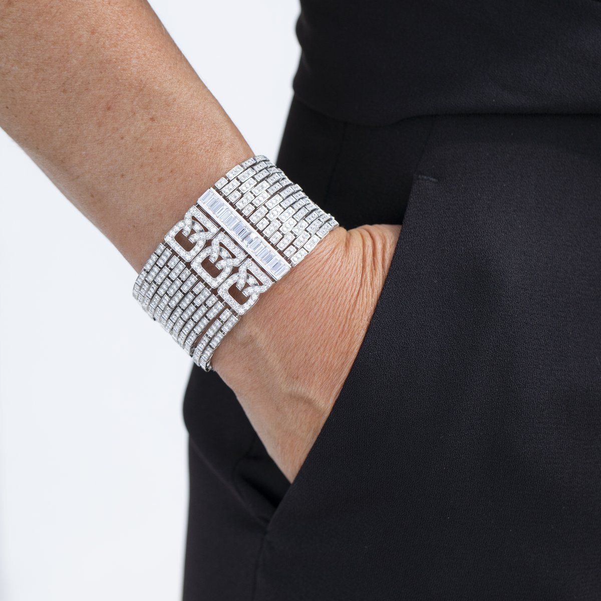 Wide baguette and round diamond cuff bracelet worn with a black outfit, hand in pocket