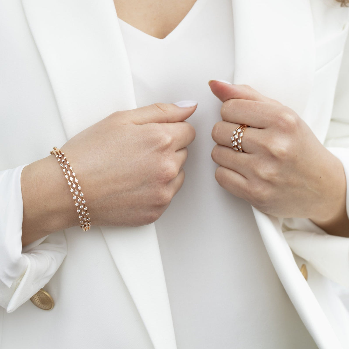 Hands in a white blazer wearing a rose gold Wave diamond bracelet and ring