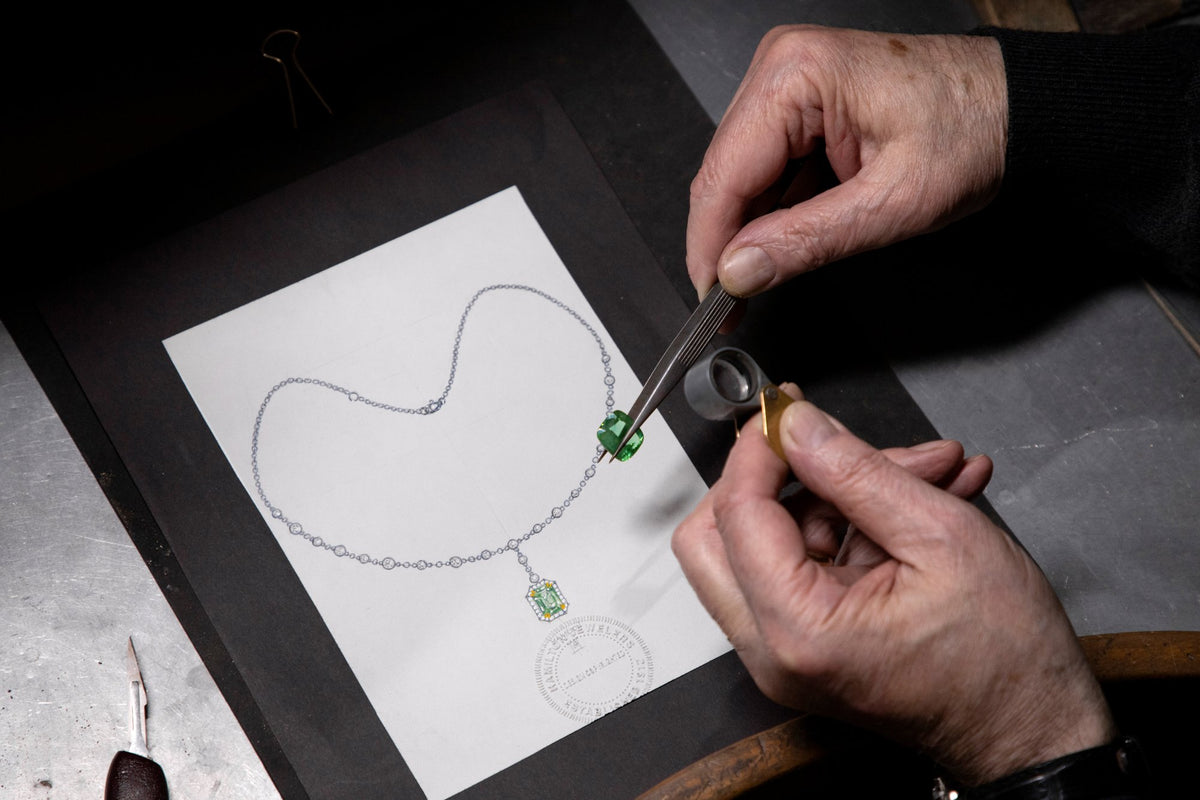 Designer reviewing a necklace sketch with a loose emerald
